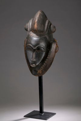un masque en bronze posé sur un socle noir, avec un fond gris