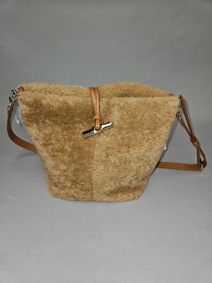 beige purse with brown leather strap and handle on grey background