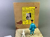 une petite figurine représentant un homme et un chien devant une affiche