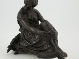 an antique bronze figurine of a woman sitting on a tree stump