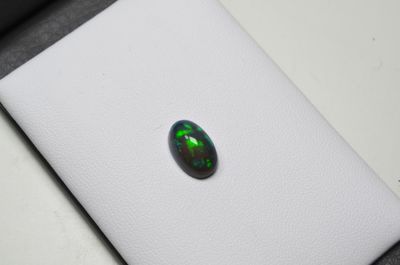 une pierre oplite ovale de couleur verte, posée sur une surface blanche