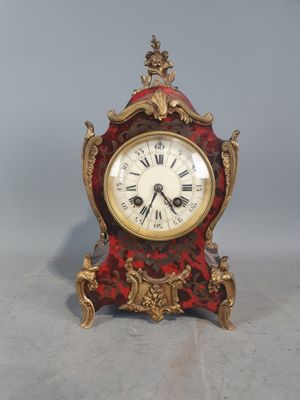 une horloge rouge et dorée posée sur une surface grise