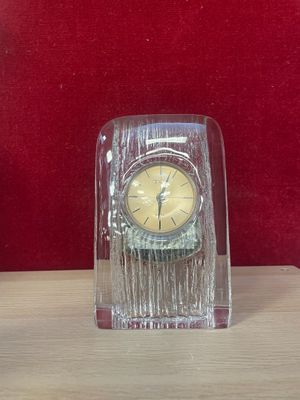 a small glass clock on a table with a red background