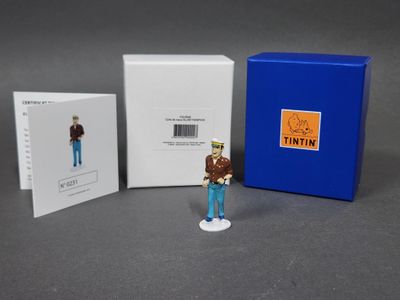 La figurine se tient à côté d'une boîte bleue et d'une boîte blanche.