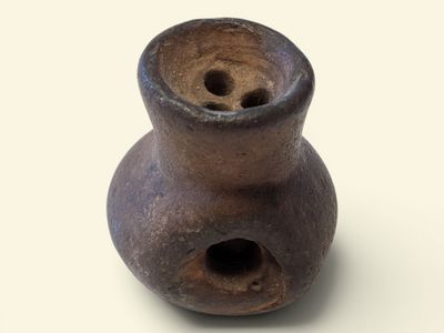un vase marron percé d'un trou, posé sur une surface blanche
