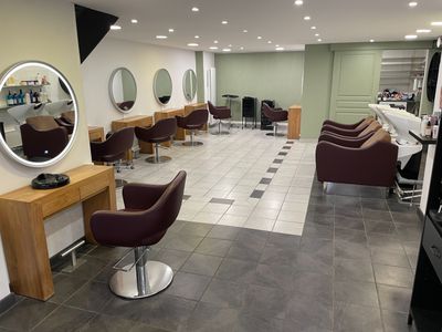 une photo d'un salon de coiffure avec des fauteuils et des miroirs
