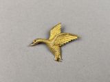un gros plan d'une broche en forme de colibri doré posée sur une surface blanche