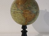 un petit globe posé sur un socle noir, lui-même posé sur une surface blanche