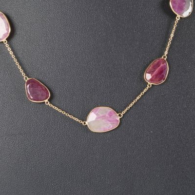 a necklace with pink stones and gold chains on a mannequin