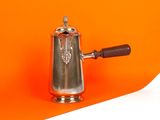 une cafetière en argent avec une poignée en bois sur fond orange