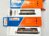 trois trains miniatures sont rangés dans des boîtes posées sur une surface blanche