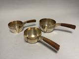 three brass measuring cups with wooden handles on a white surface