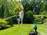 Cet homme arrose la pelouse du jardin avec un tuyau d'arrosage.