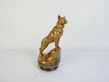 statue en laiton représentant un chien assis sur un rocher, sur fond blanc