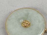 a close up of a gold and jade pendant on a white surface