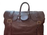 the large brown leather bag is sitting on a white surface
