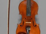 un vieux violon avec un archet et un repose-archet posé sur une surface grise