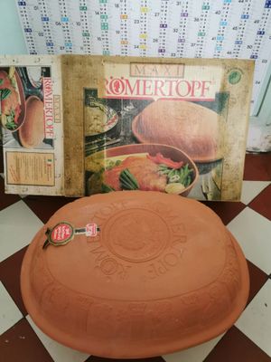 un grand faitout en terre cuite posé sur un sol à carreaux, à côté d'un livre de cuisine
