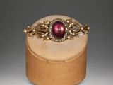 a close up of a gold and red broocher on a wooden stand