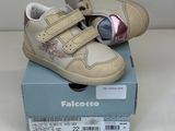 des chaussures de bébé beiges et roses dans une boîte posée sur une surface blanche