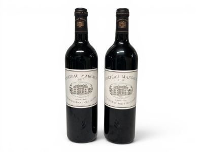 two bottles of red wine sitting next to each other on a white surface