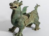 une vieille figurine en bronze représentant un dragon sur fond blanc