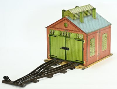 un petit train miniature avec une porte verte et un bâtiment rouge