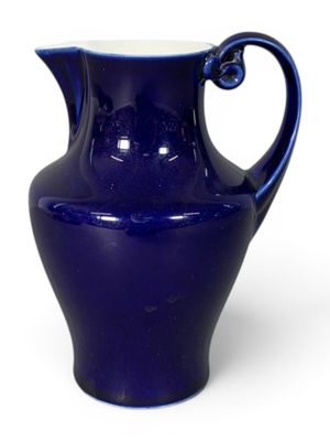 purple glass pitcher with a curved handle on a white background