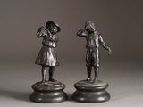 pair of bronze figurines of a boy and a girl on pedestals