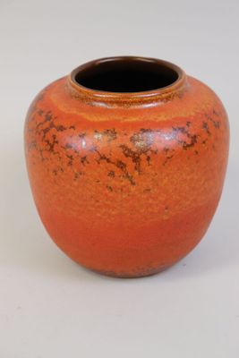 un vase orange posé sur une table, sur fond blanc