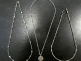 two silver necklaces on a black surface with a white background