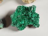 three pieces of green mineral on a white surface next to some rocks