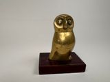 figurine en or représentant un hibou, posée sur un socle en bois, sur fond blanc