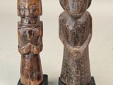 deux figurines en bois représentant un homme et une femme, posées sur des socles noirs