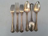 cinq cuillères en argent et une fourchette sur une table