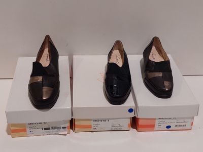 trois paires de chaussures noires posées sur des cartons, sur une surface blanche