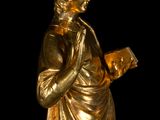 gold statue of a man holding a book in his right hand
