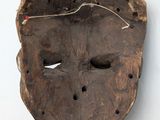 an old wooden mask hanging on a wall with a red string