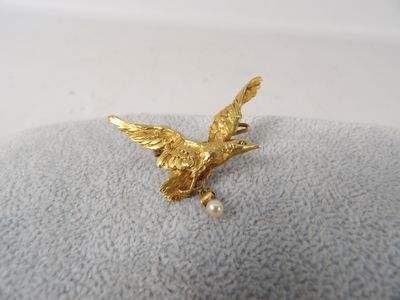 une photo représentant une broche en forme d'oiseau de couleur dorée posée sur une couverture grise