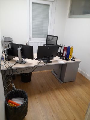 a desk with two computer monitors and a trash can in front of it