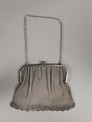 un sac à main en métal argenté muni d'une bandoulière en chaîne, accroché à un mur blanc