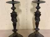 une paire de bougeoirs anciens noirs posés sur une table en bois, avec un mur en arrière-plan