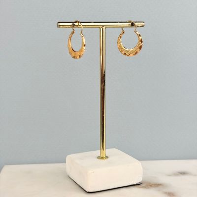 une paire de boucles d'oreilles créoles en or posée sur un socle en marbre