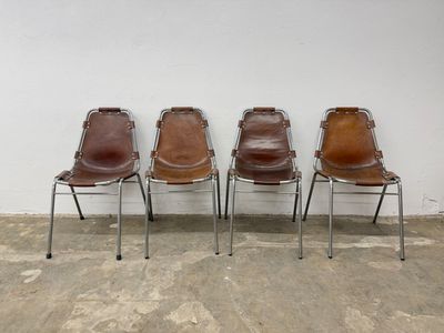 three brown leather chairs sitting next to each other in front of a white wall