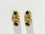 une paire de boucles d'oreilles en or ornées de pierres bleues, posées sur un fond blanc