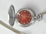 a silver pocket watch with a red face and a chain