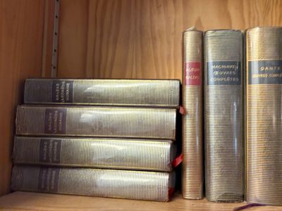 Plusieurs livres sont empilés sur une étagère en bois dans une bibliothèque