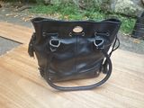 black leather handbag sitting on a wooden table in front of a stone wall