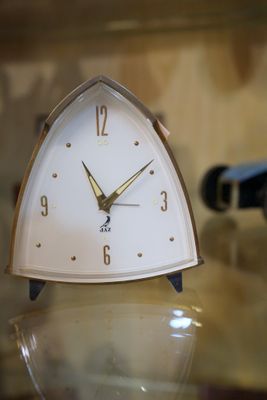 une horloge blanche posée sur une table en verre, avec une bouteille de vin en arrière-plan