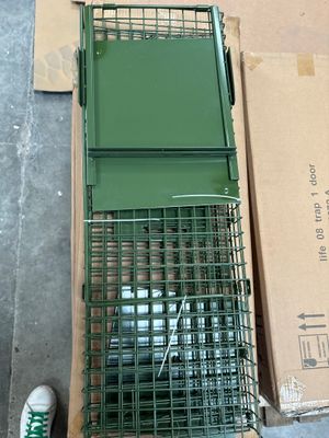 a green cage with a bird inside of it on the ground
